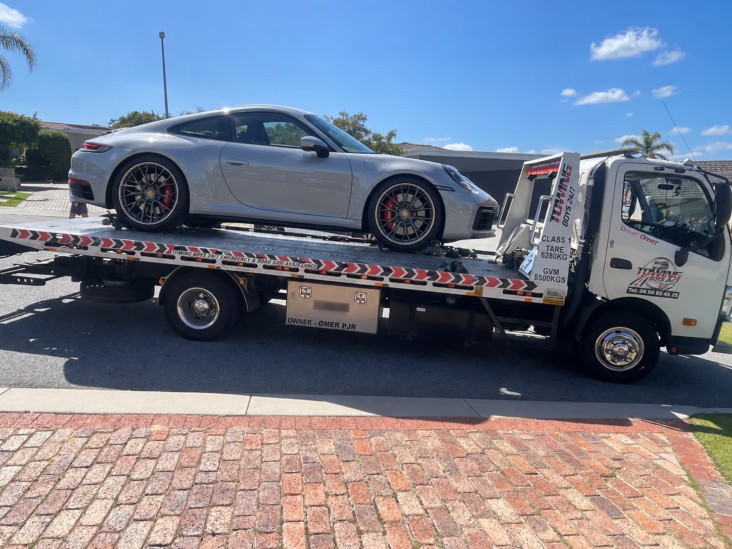 Towing Boys 24/7 flatbed tow truck carrying a silver Porsche 911 on a Perth residential street
