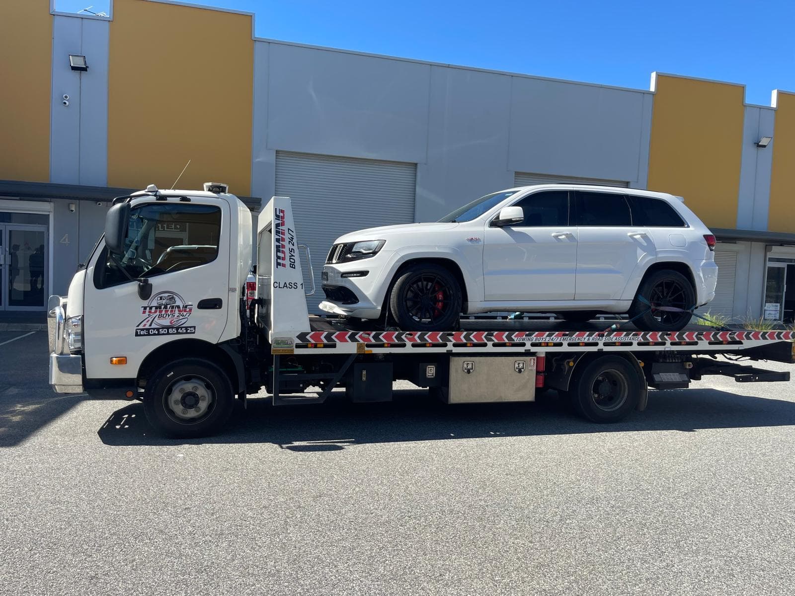Towing Boys 24/7 truck transporting a white Jeep Grand Cherokee SRT through a Perth industrial estate