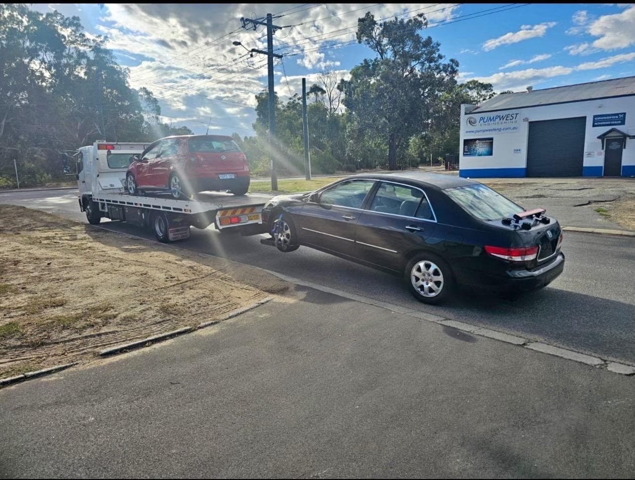 Towing Boys 24/7 truck towing a sedan on the road while carrying a hatchback on the tray