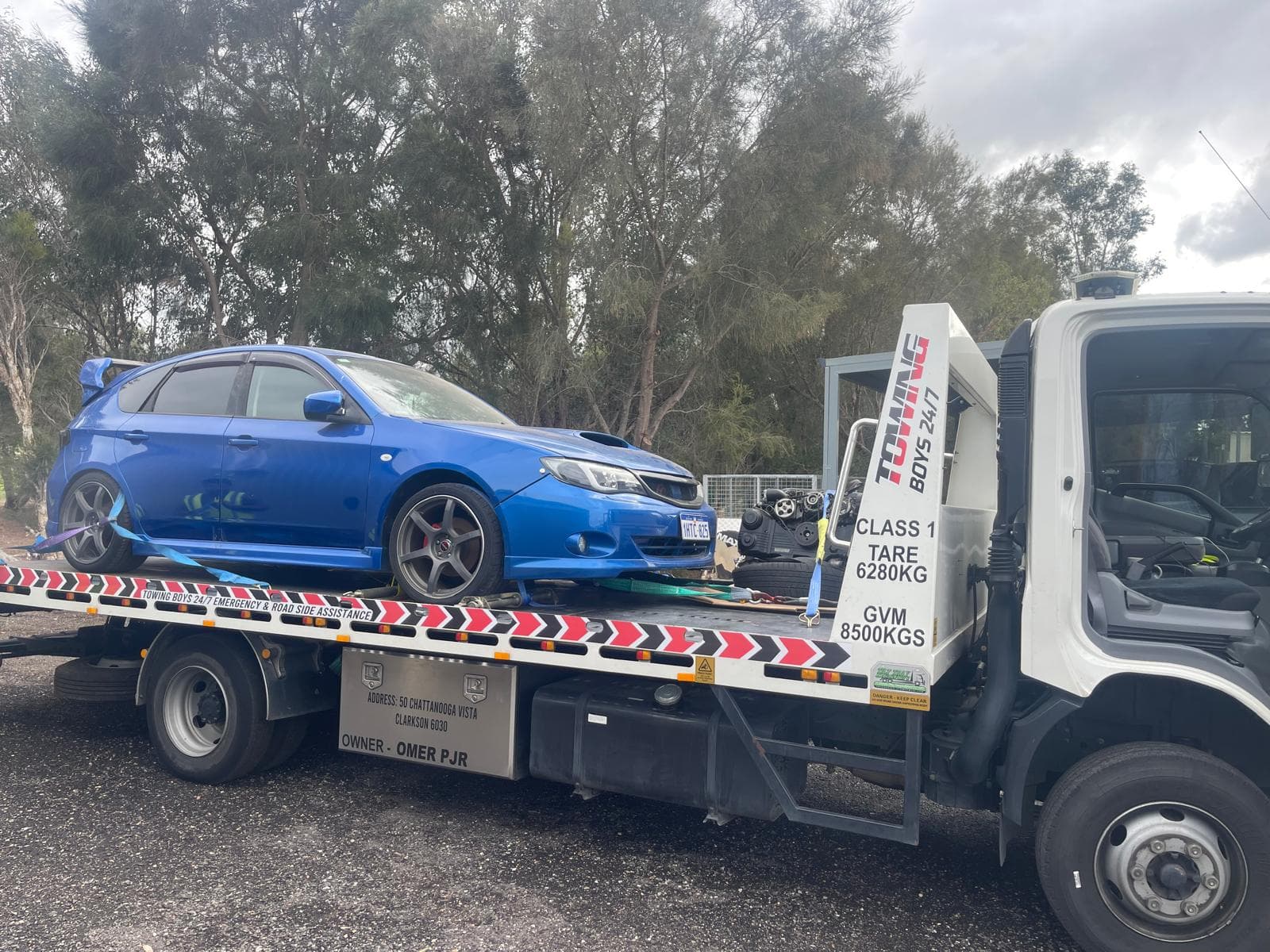 Towing Boys 24/7 truck transporting a damaged Subaru WRX hatchback and recovered engine parts