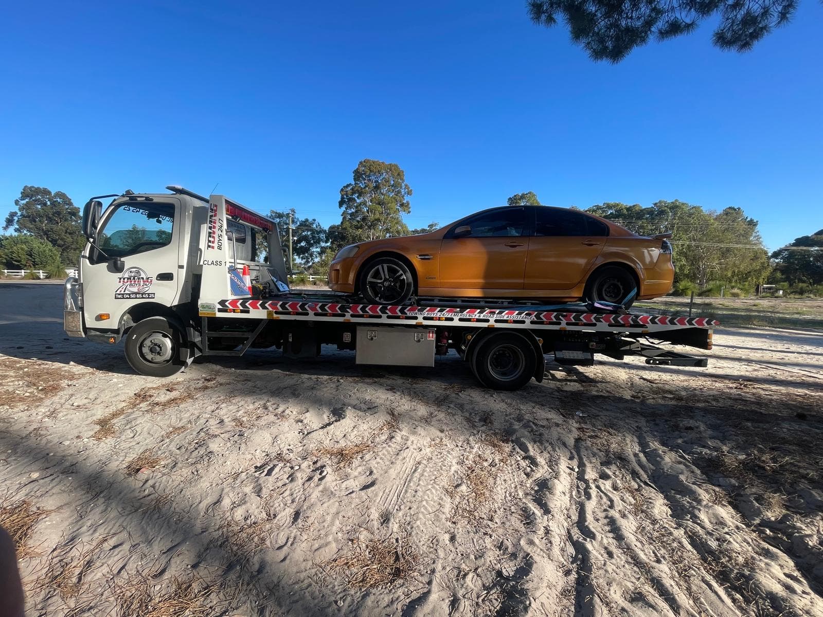 Towing Boys 24/7 truck transporting an orange Holden Commodore through Perth bushland